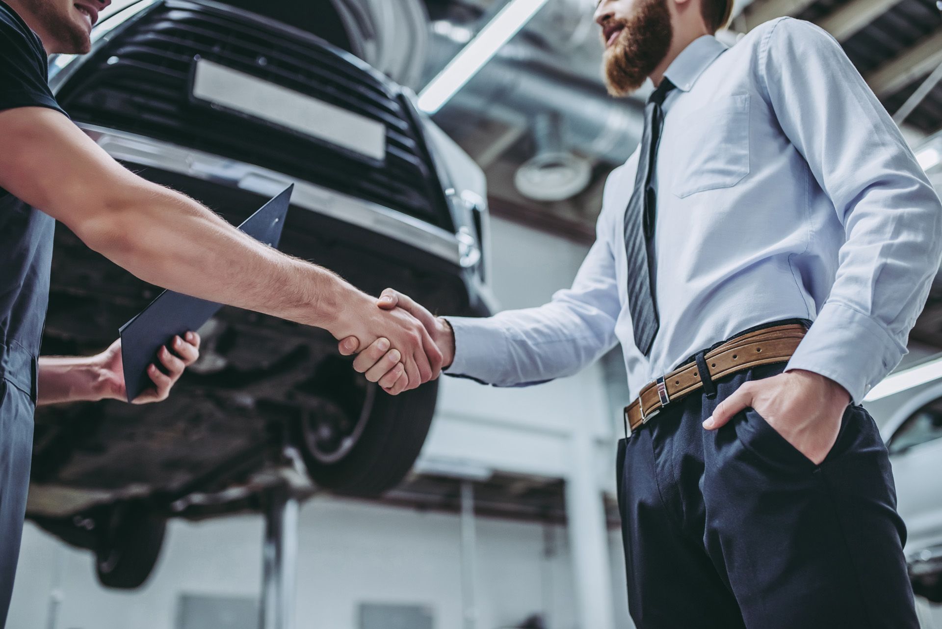 Zwei Menschen geben sich einen Handschlag vor einem angehobenen Auto